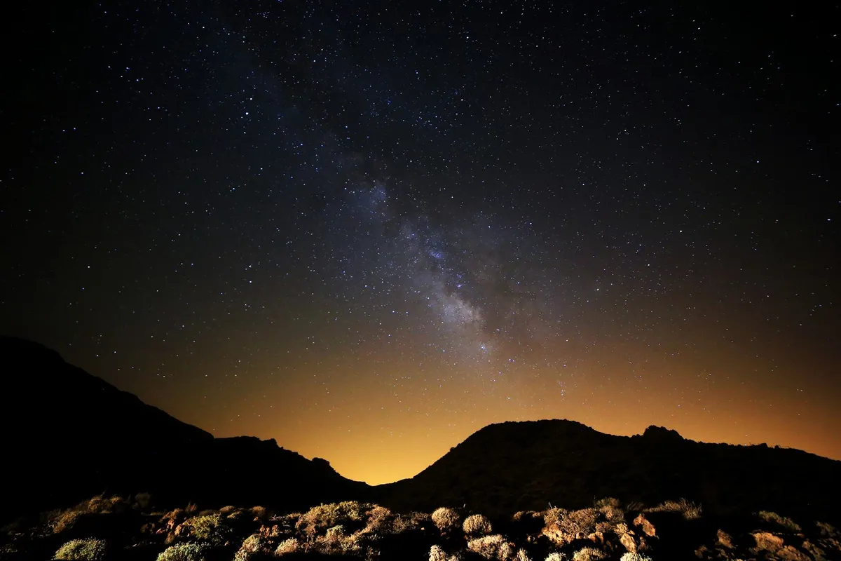 The Milky Way arching over dark mountain silhouettes on a clear night