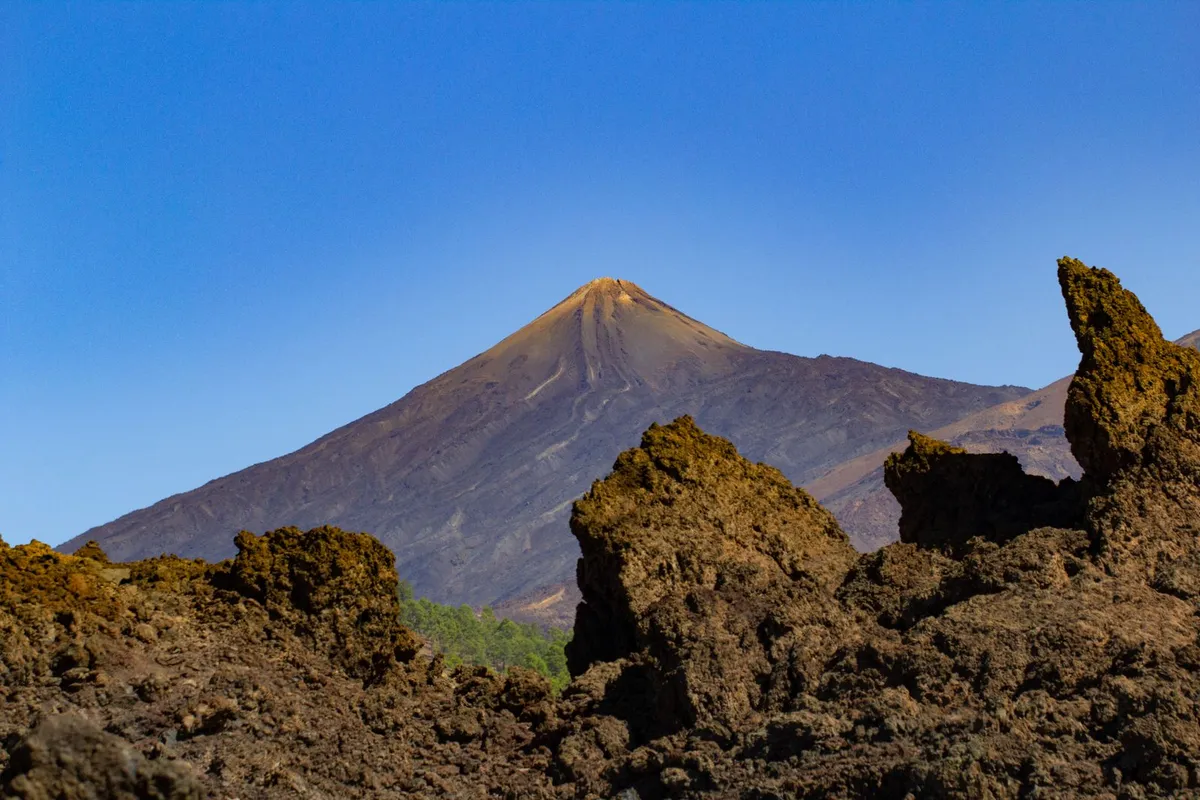 Mount Teide's volcanic cone rising above dark lava terrain under a clear sky in Teide National Park