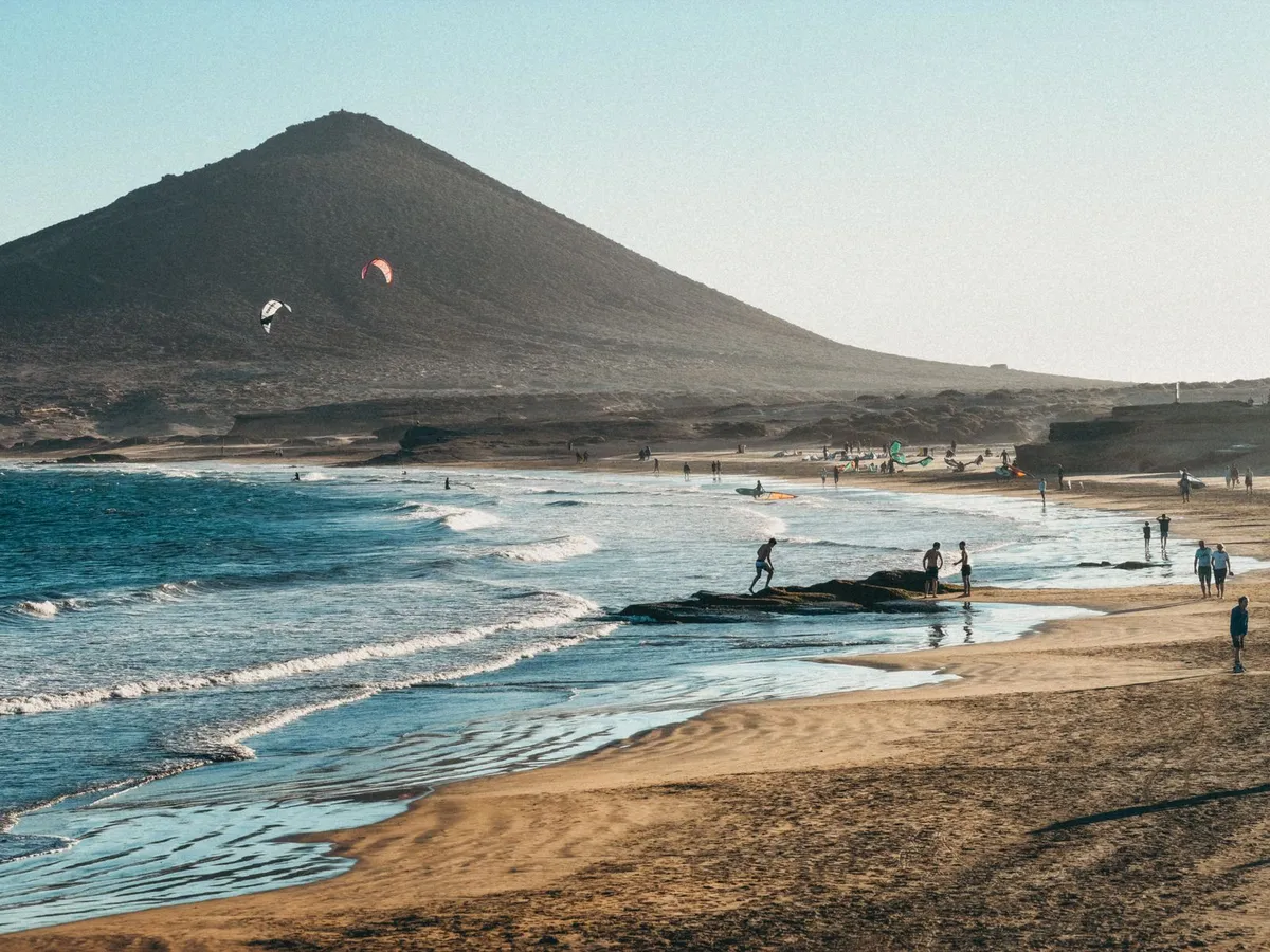 Kite surfers and beachgoers below the Montaña Roja cone at El Médano on Tenerife's south coast.
