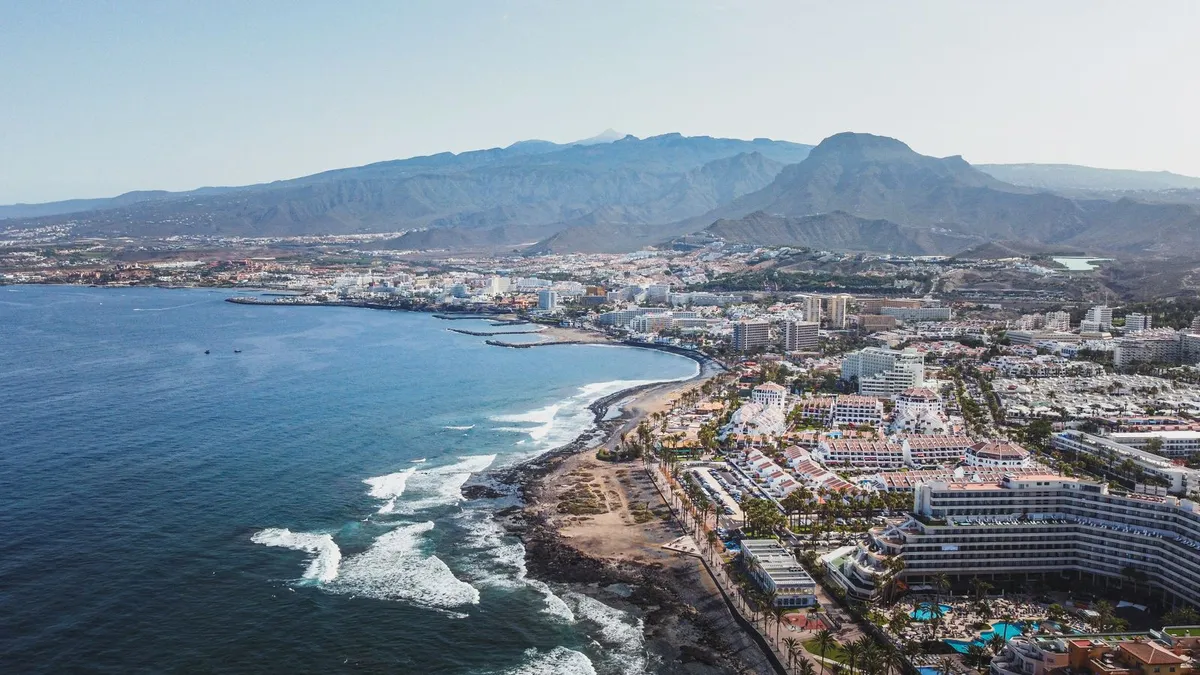 Aerial view of the south Tenerife resort coastline, with beachfront hotels and mountains behind