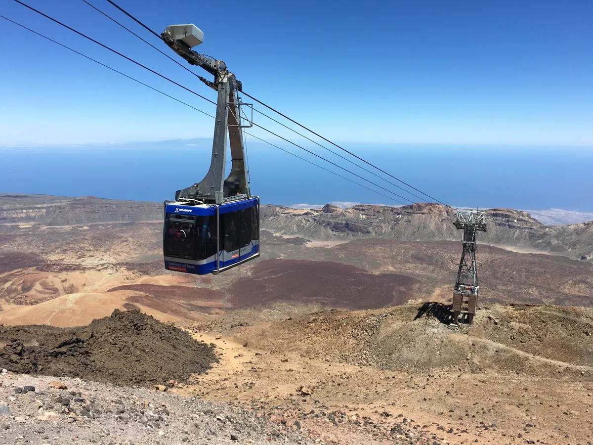 A cable car cabin descending over the volcanic crater of Teide, with the ocean horizon far below
